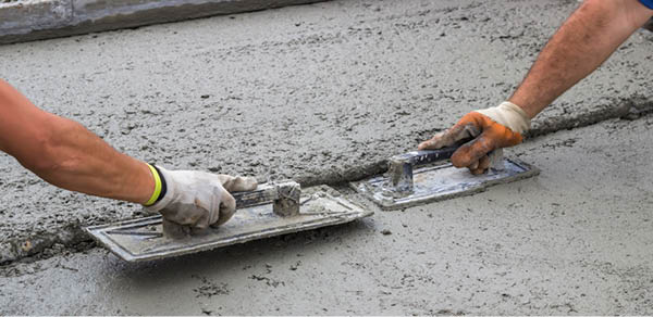 Leveling concrete with trowels, mason hands spreading poured concrete. Selective focus.