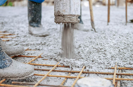 Manual workers pouring cement through pipe on roof.