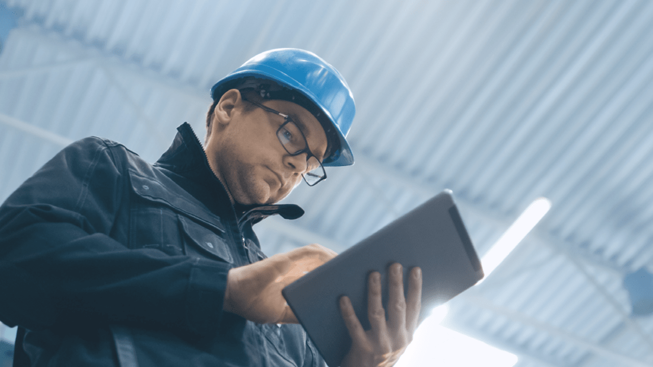 Factory worker in a hard hat is using a tablet computer.