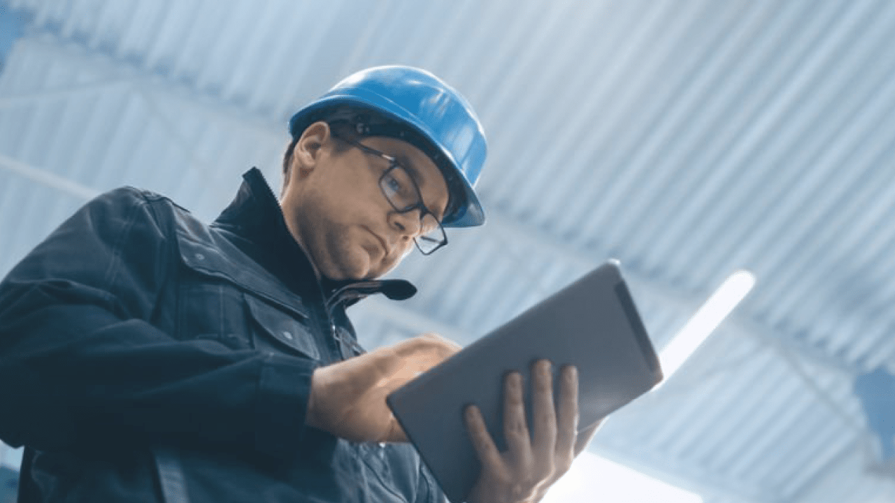 Factory worker in a hard hat is using a tablet computer.