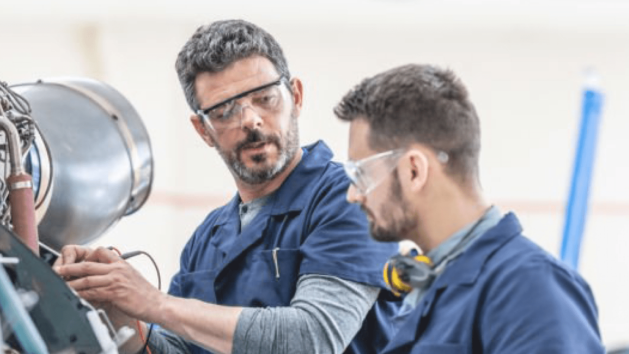 Young aviation mechanics studying to repair engine medium shot. Helicopter hangar workers in protective equipment examining jet, side view