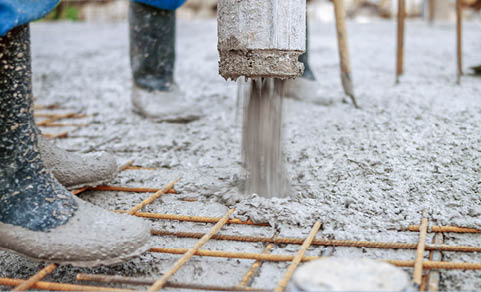 Manual workers pouring cement through pipe on roof.